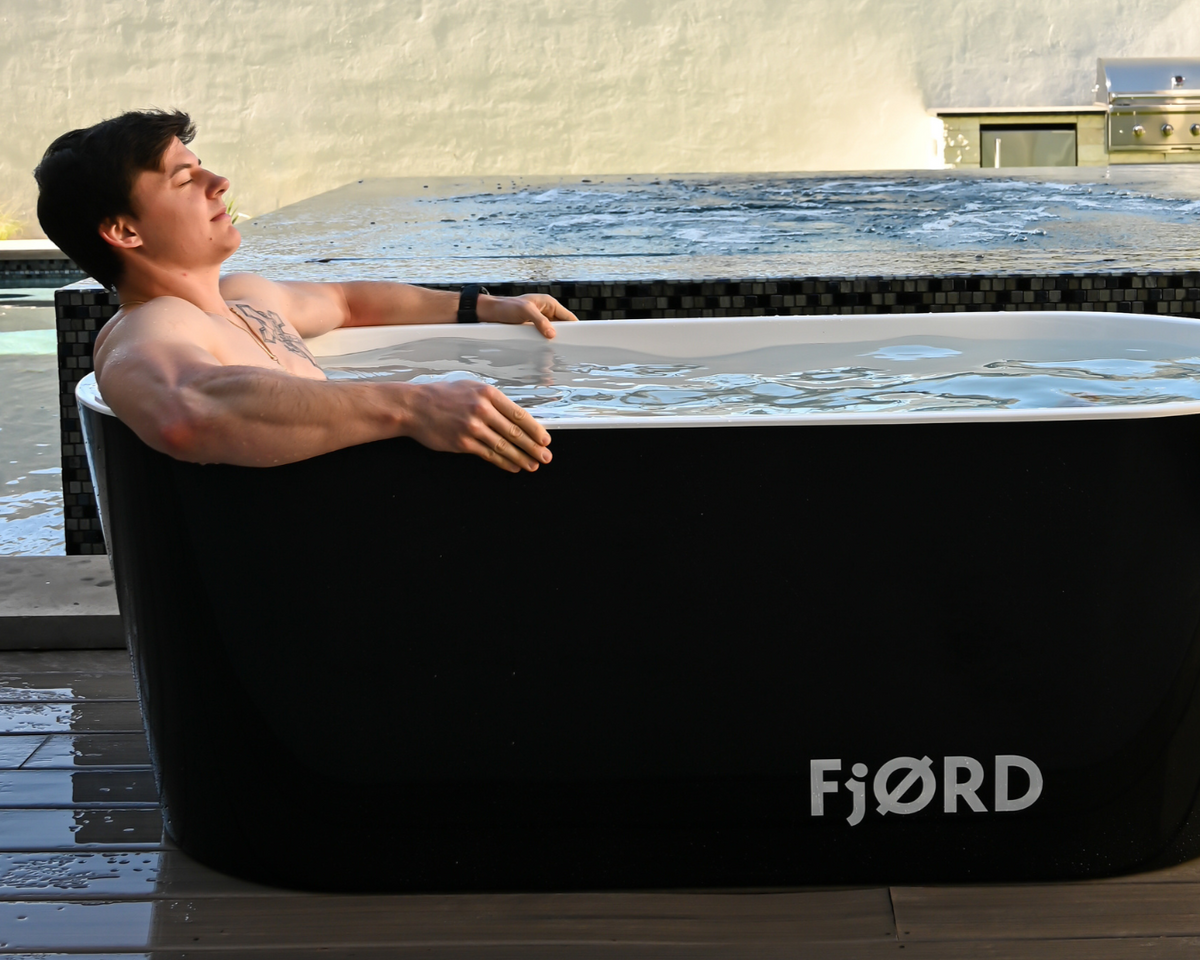 Man sitting in a black FjØRD cold plunge beside a pool