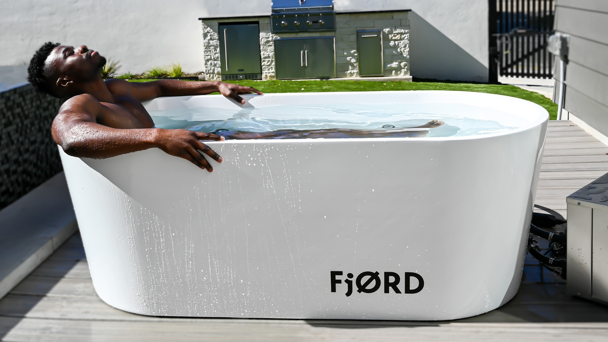 Man resting his arms on the rim of a white FjØRD cold plunge outdoors